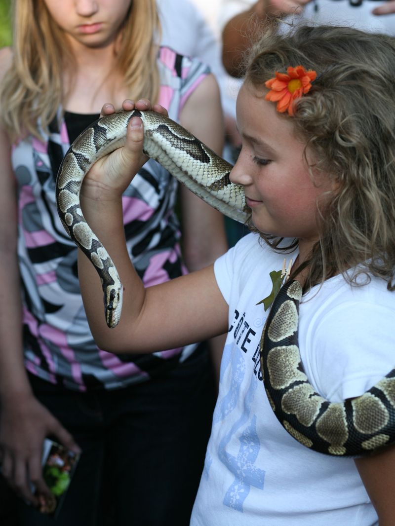 Ein Mädchen mit braunen Locken und einer roten Blume im Haar hält eine Schlange.