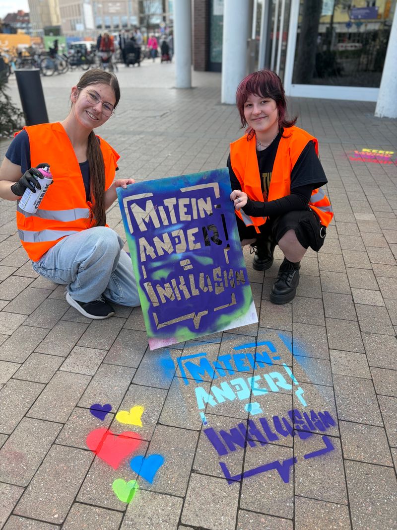 Zwei Mädchen halten eine Schablone und eine Sprühdose in der Hand. 