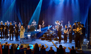 Musikerinnen und Musiker stehen mit Instrumenten auf einer Bühne.