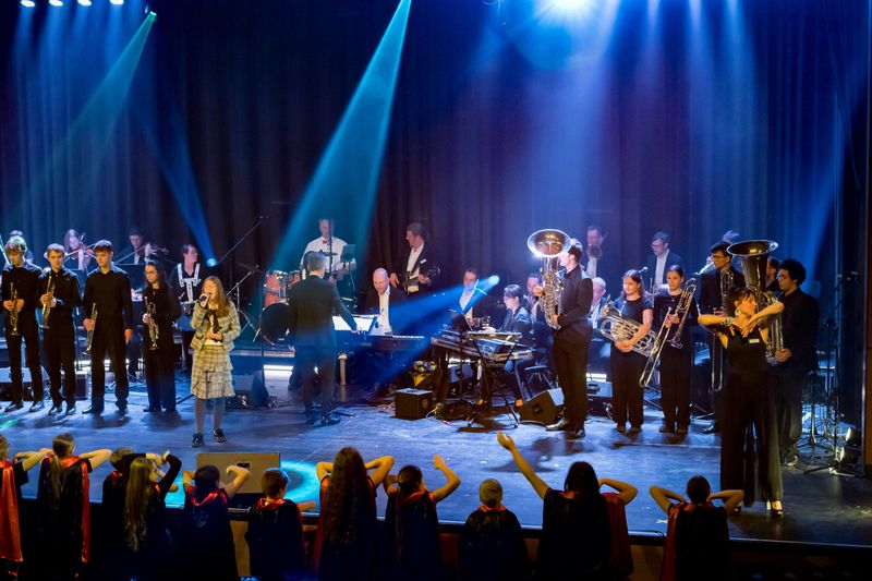 Musikerinnen und Musiker stehen mit Instrumenten auf einer Bühne.