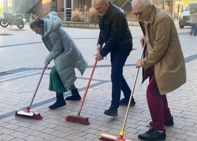 Drei Personen, die im öffentlichen Raum einen Platz kehren.