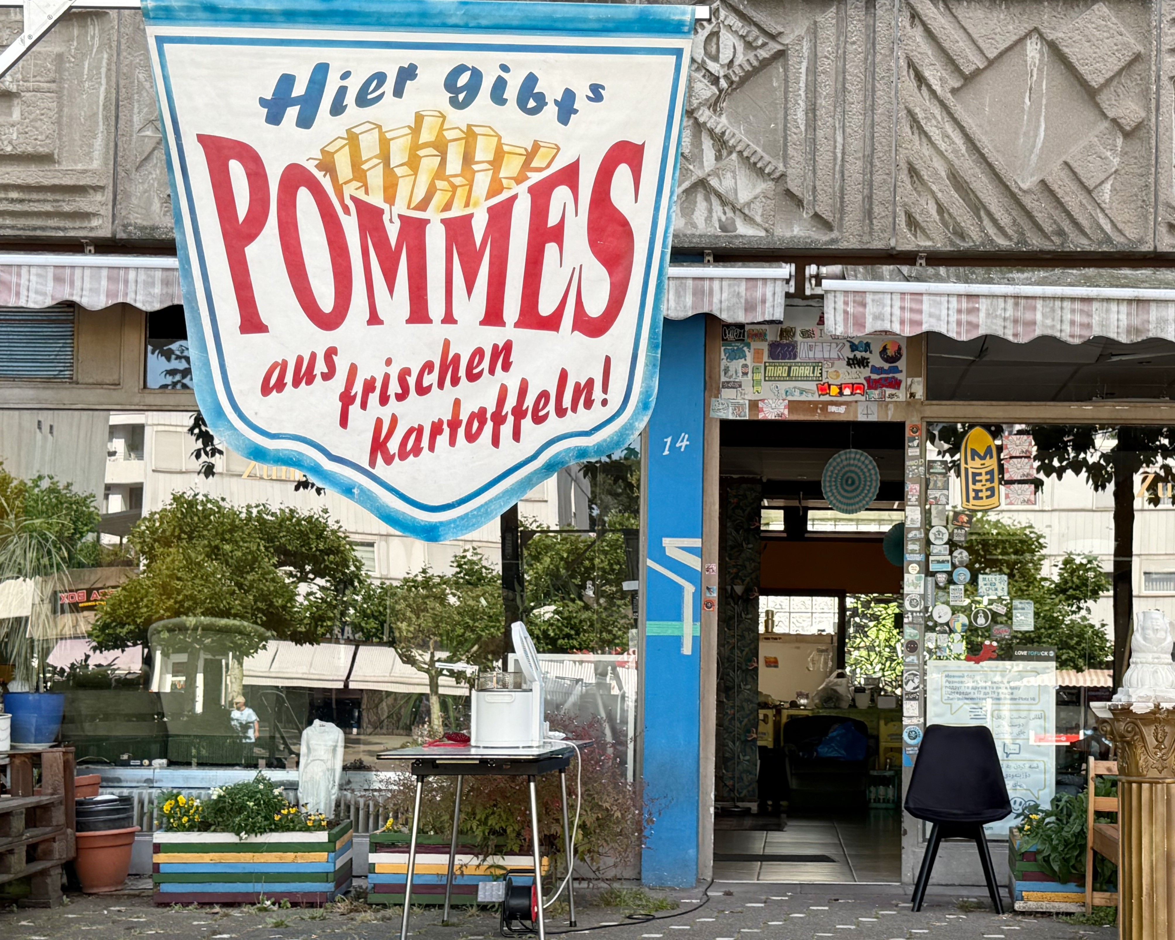 Blick von außen auf eine Ladenzeile. Vor einem Laden hängt ein großes Banner mit der Aufschrift 