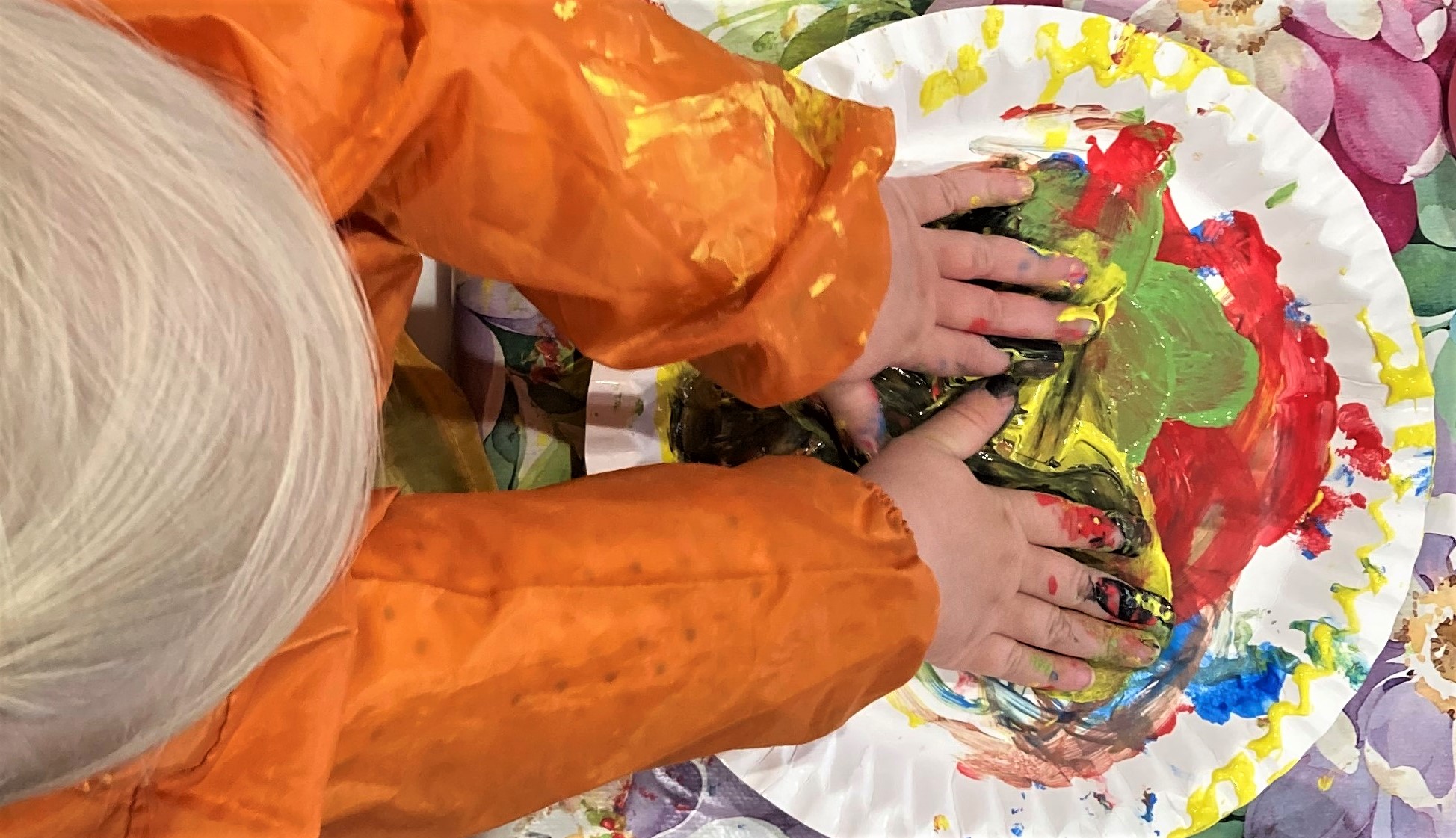 Ein Kind taucht seine Hände in bunte Farben, die auf einem Pappteller sind.