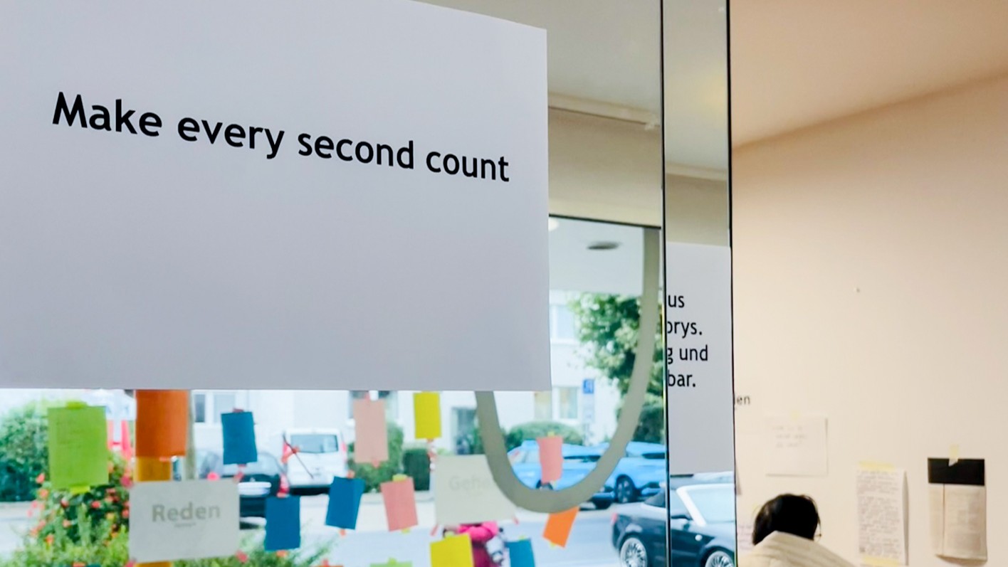 Blick durch eine Glasscheibe eines Ladenlokals von innen nach außen. Auf der Scheibe hängen kleinere, bunte Zettel. Vorne hängt ein weißer, großer Zettel mit dem Satz 