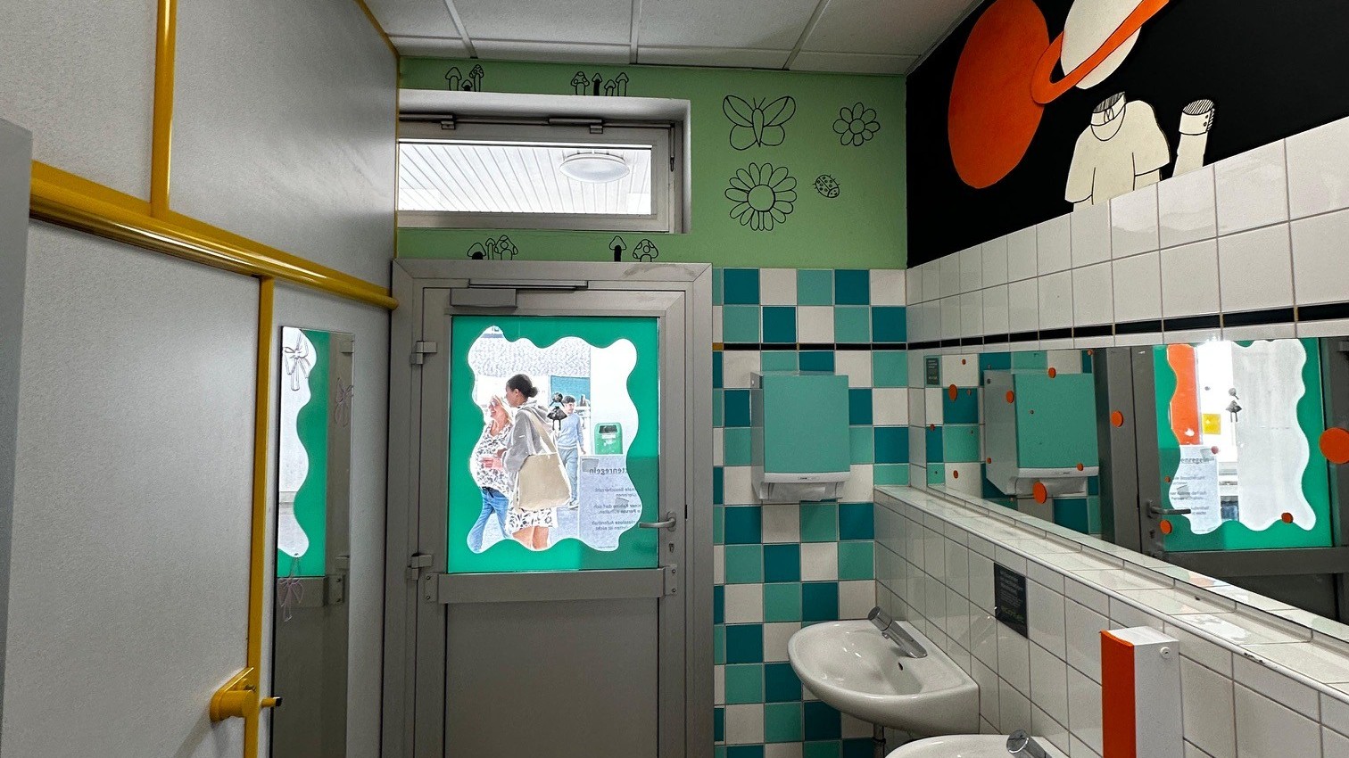 Blick in einen Waschraum. Die Fliesen und Wände sind bunt angemalt mit Farben, Blumen und Weltraummotiven.