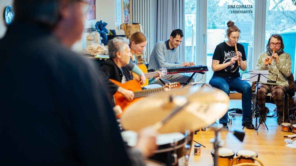 Mehrere Menschen sitzen in einem Halbkreis und spielen auf verschiedenen Instrumenten.